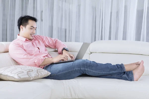 Jonge man ontspannen op de Bank met laptop — Stockfoto