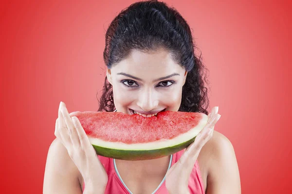 Jonge vrouw bijten watermeloen op rode achtergrond — Stockfoto