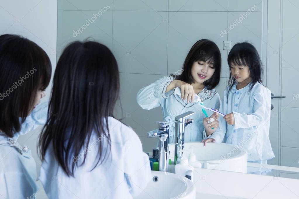 Young mother and daughter brush teeth 