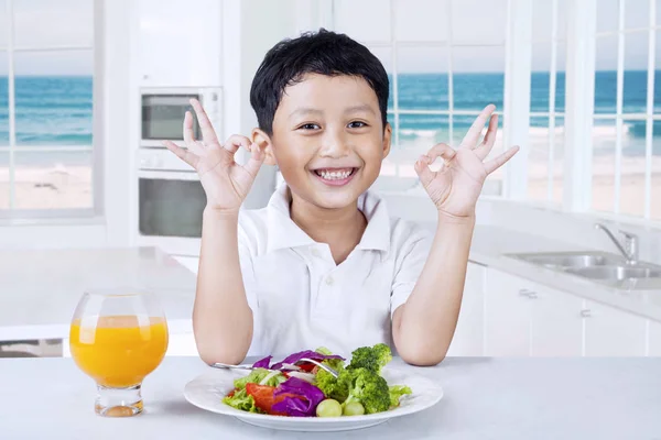 Menino feliz com salada na cozinha — Fotografia de Stock