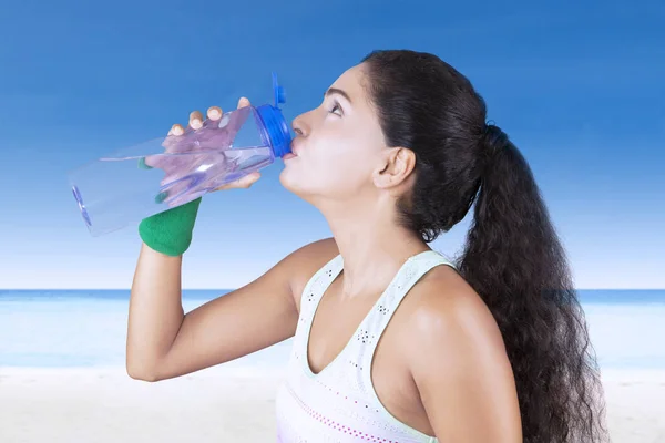 Une jeune femme boit de l'eau à la plage — Photo