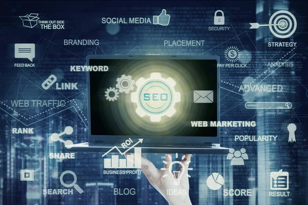 La mano sostiene el ordenador portátil con el icono SEO — Foto de Stock