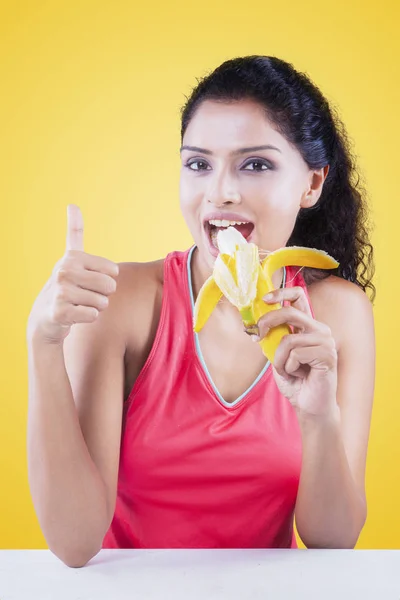 Vrouw die het eten van een banaan op gele achtergrond — Stockfoto