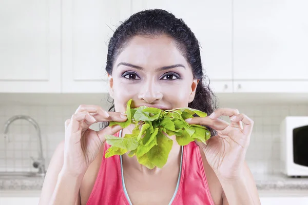 Zdravá žena kousání špenát v kuchyni — Stock fotografie