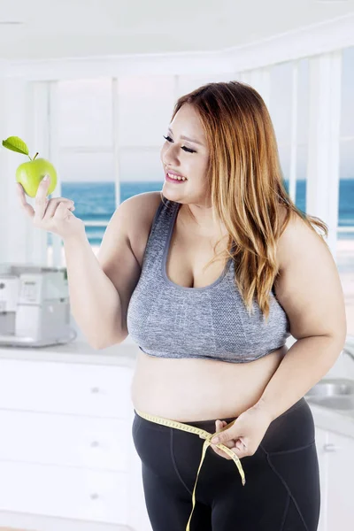 Obese woman holds apple in kitchen — Stock Photo, Image