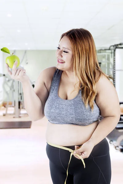 Tlustá žena drží jablko v tělocvičně — Stock fotografie
