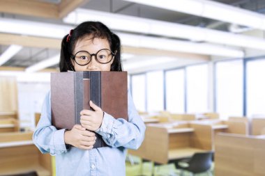 Küçük kız sınıfta kitap arkasına saklanmış 