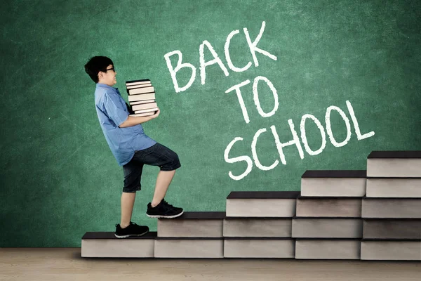 Schoolboy carrying pile of books on stair — Stock Photo, Image