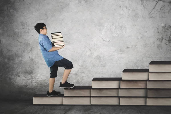 Schoolboy carrying pile of books on staircase — Stock Photo, Image