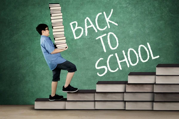 Schoolboy carrying stack of books on stair — Stock Photo, Image