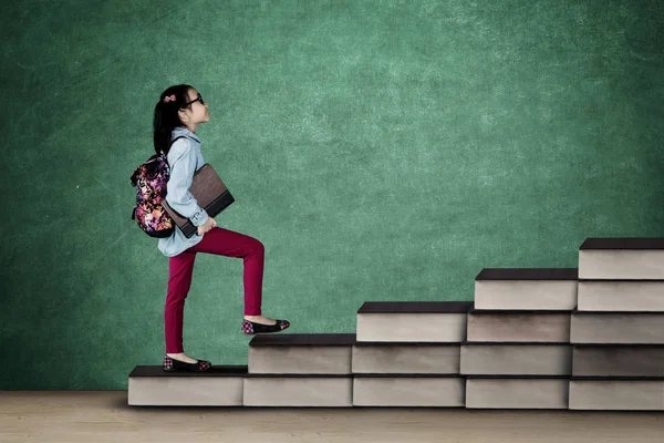 Colegiala sosteniendo un libro en la escalera de libros — Foto de Stock