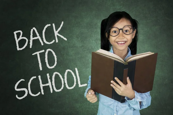 Colegiala sosteniendo libro en el aula — Foto de Stock