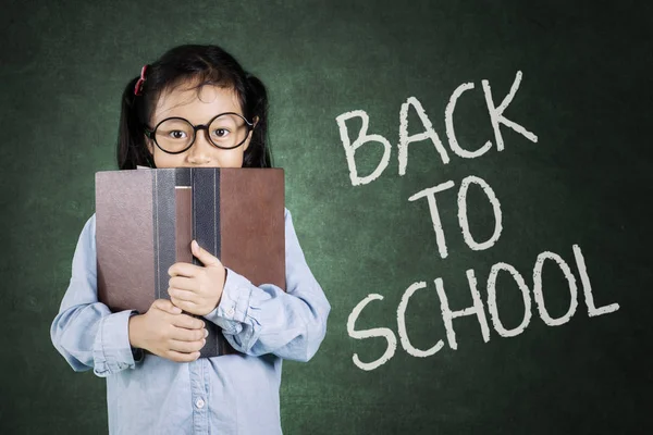 Schoolgirl looking at camera behind book — Stock Photo, Image