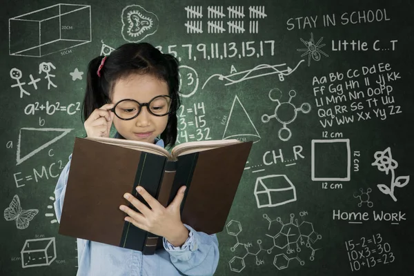 Schoolgirl reading book in classroom — Stock Photo, Image