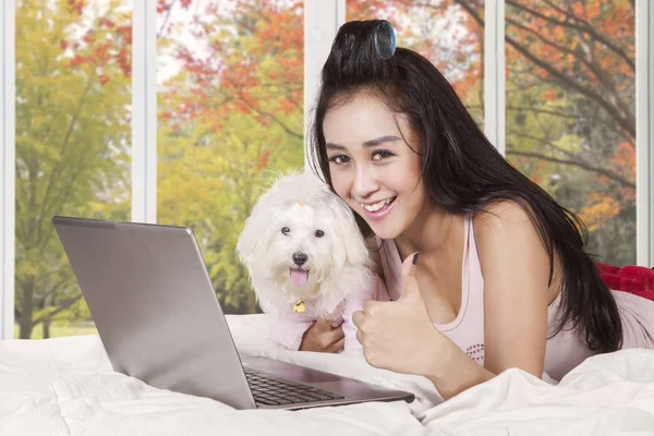 Girl showing thumb up on the bed with her dog — Stock Photo, Image