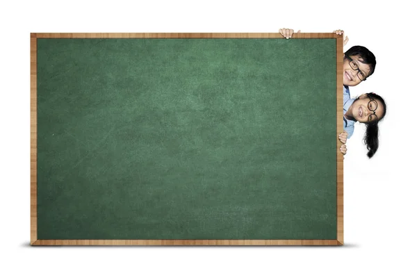 Primary students hiding behind chalkboard — Stock Photo, Image