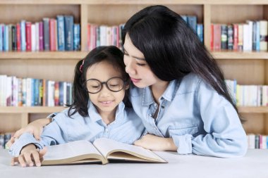 Öğretmen bir ders kitabı okumak için onun öğrenci yardımcı olur.