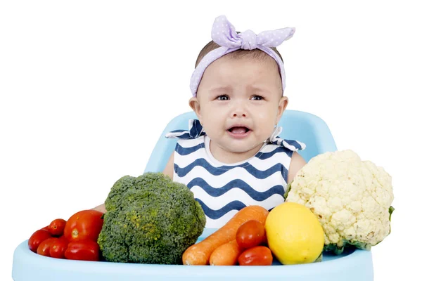 Söt baby gråter med grönsaker på stol — Stockfoto