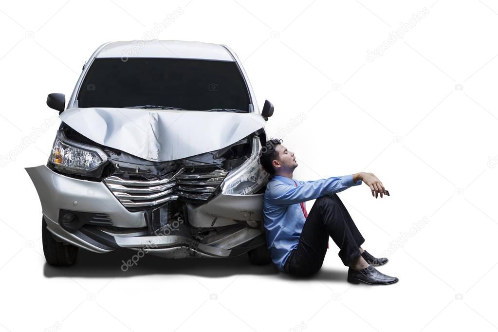 Frustrated businessman sits next to damaged car