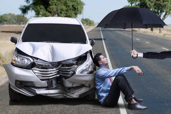 Человек, сидящий рядом с помятой машиной
