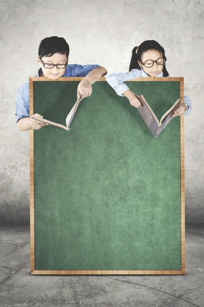 Estudiantes leyendo libros detrás de una pizarra — Foto de Stock