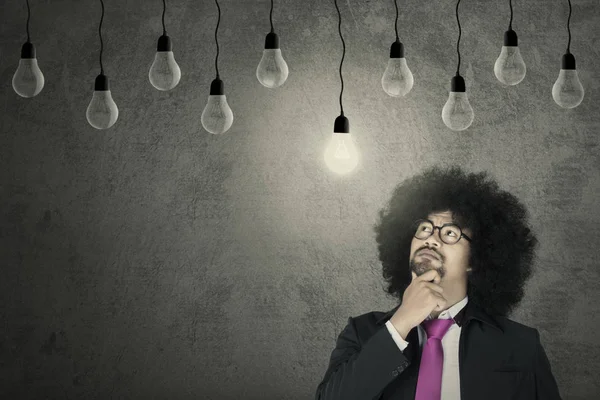 Afro businessman looking at light bulb — Stock Photo, Image