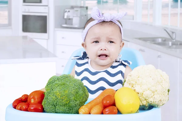 Bebê triste com legumes na cozinha — Fotografia de Stock
