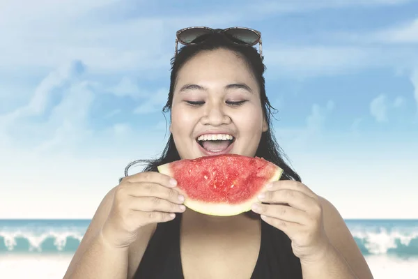 Obese woman eating watermelon on beach — Stock Photo, Image
