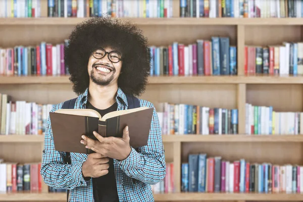 Αφρο φοιτητής κρατώντας το βιβλίο στη βιβλιοθήκη — Φωτογραφία Αρχείου