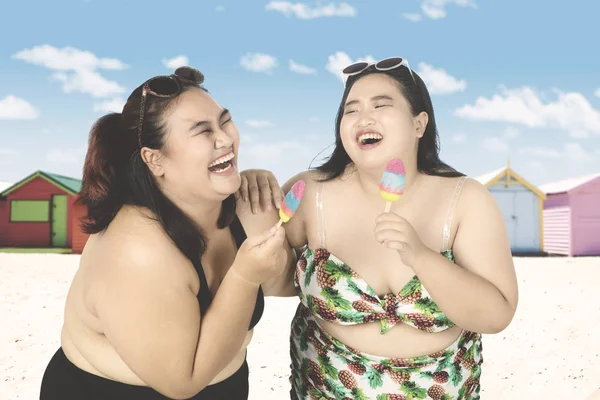Vrolijke vrouwen eten ijs op strand — Stockfoto