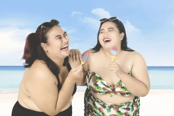 Vrolijke vrouwen eten ijs op strand — Stockfoto
