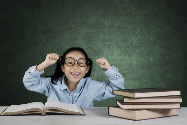 Улыбающаяся девушка поднимает руки с книгами в классе — стоковое фото