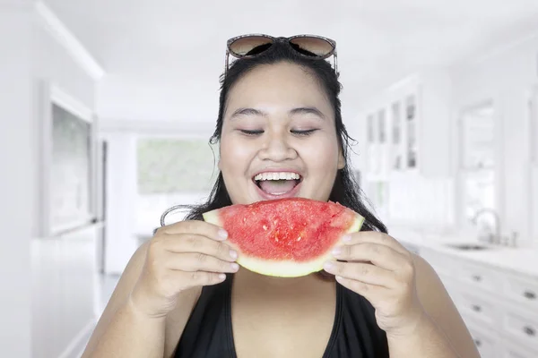 Dikke vrouw eet watermeloen in keuken — Stockfoto