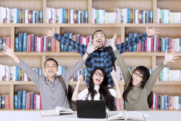 Estudantes alegres levantam as mãos na biblioteca — Fotografia de Stock