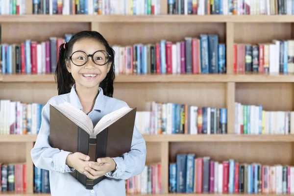 Lindo niño sonriendo con libro en la biblioteca — Foto de Stock