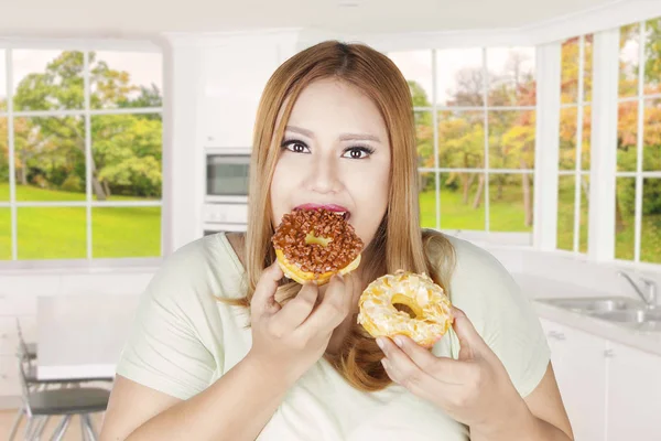 뚱뚱한 여자 두 도넛 집에서 먹는 — 스톡 사진