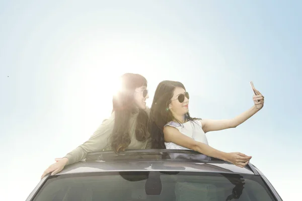 Dos mujeres con teléfono inteligente en el techo del coche — Foto de Stock