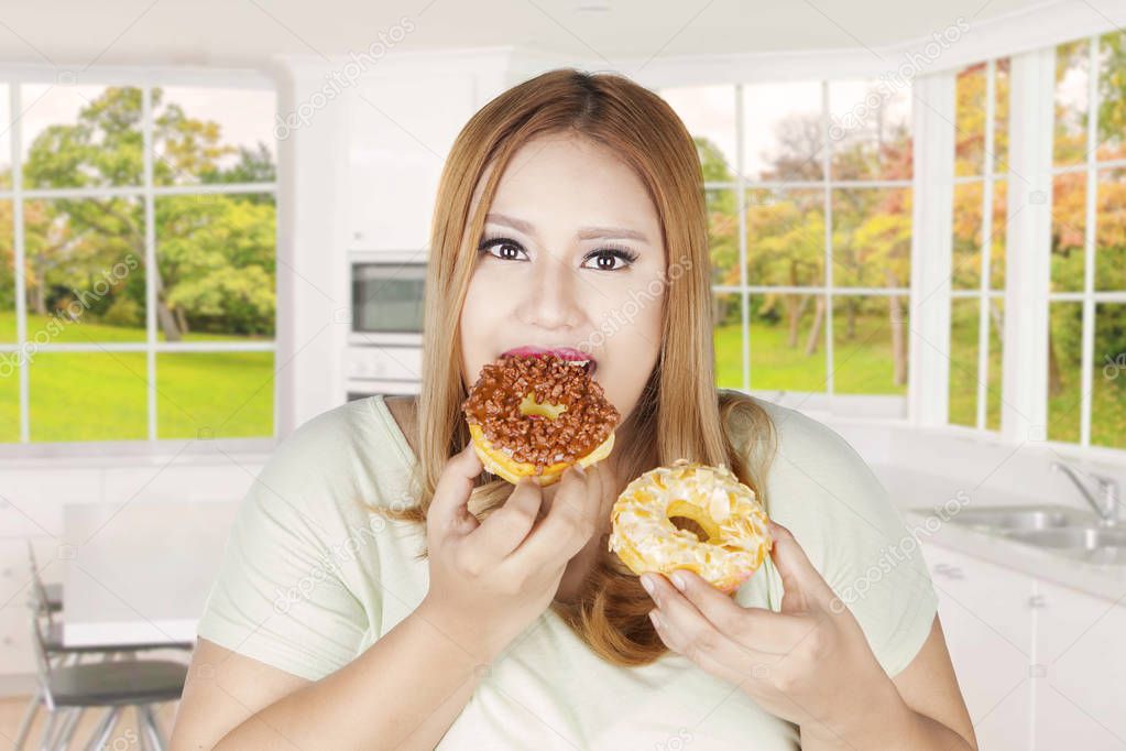 Obese woman eats two donuts at home 