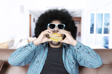Afro adam burger oturma odasında yiyor.