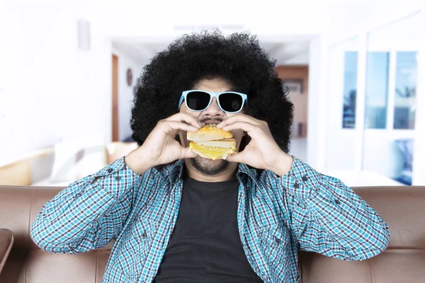 Afro ember eszik hamburgert a nappali — Stock Fotó