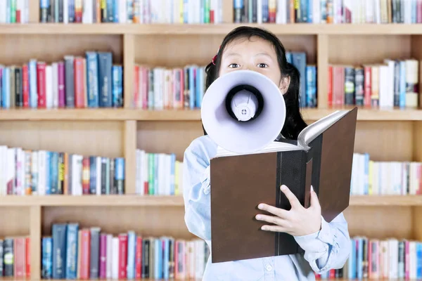 Menina bonito usando um megafone na biblioteca — Fotografia de Stock