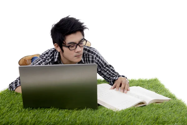 Guy reads book while using laptop on grass — Stock Photo, Image