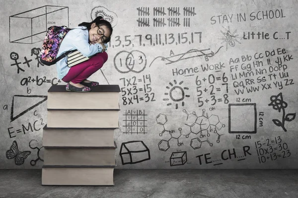 Kid squat on books with scribble at wall — Stock Photo, Image