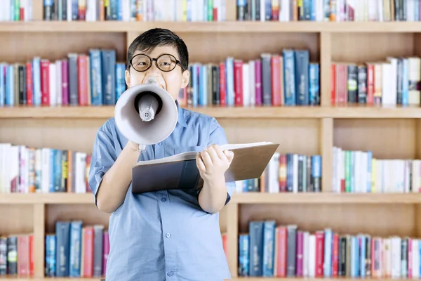 Elementary student shouting on megaphone in library — Stock Photo, Image