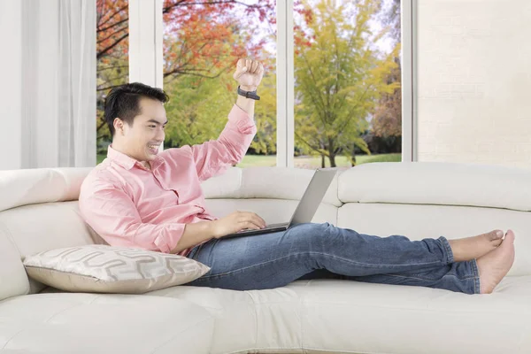 Mann hebt Hände auf Sofa mit Laptop — Stockfoto