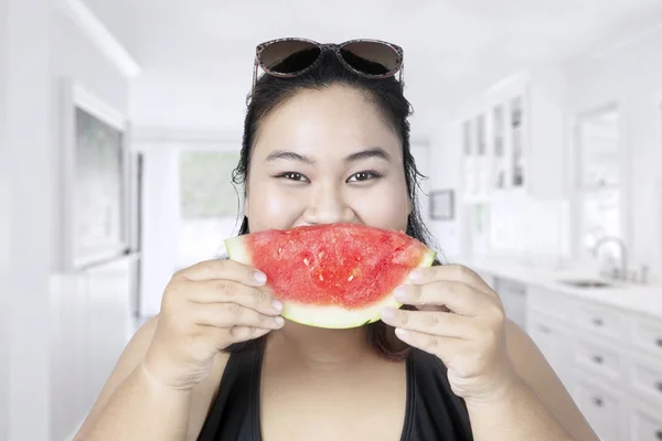Tlustá žena jíst meloun v kuchyni — Stock fotografie