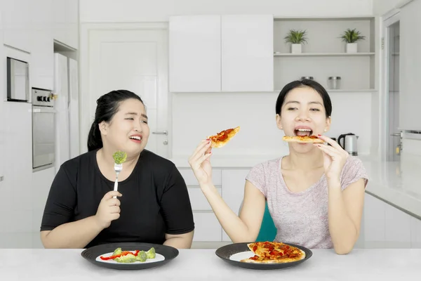 Sorgliga kvinna som tittar på hennes syster äter pizza — Stockfoto