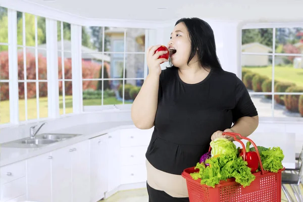 Mujer con sobrepeso comiendo una manzana en la cocina — Foto de Stock