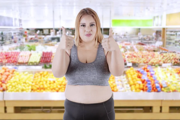 Överviktig kvinna med tummen upp i butiken — Stockfoto