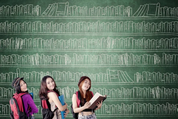 Drie vrouwelijke studenten met boeken op het schoolbord — Stockfoto